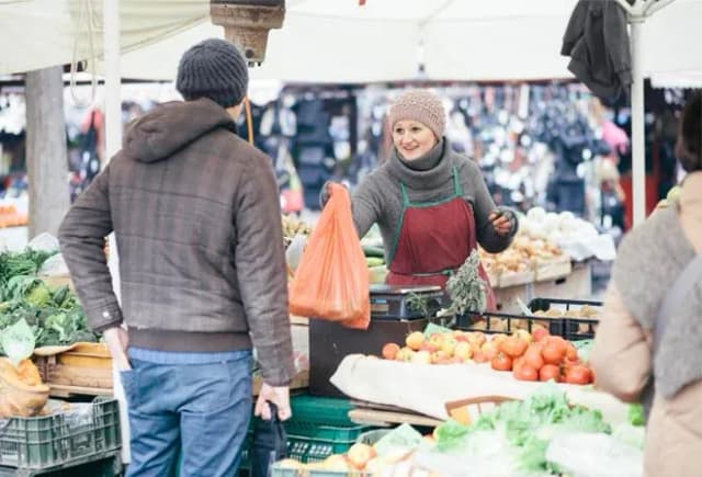 vendeuse souriante au marché échangeant avec un client devant des fruits et légumes frais