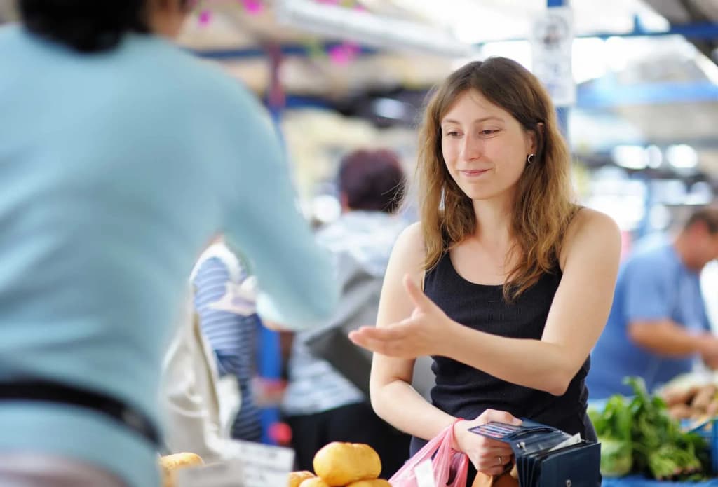 femme échangeant avec un vendeur sur un marché animé avec des fruits en arrière-plan