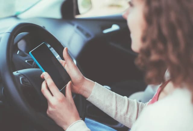 personne tenant un smartphone au volant d'une voiture avec un tableau de bord visible