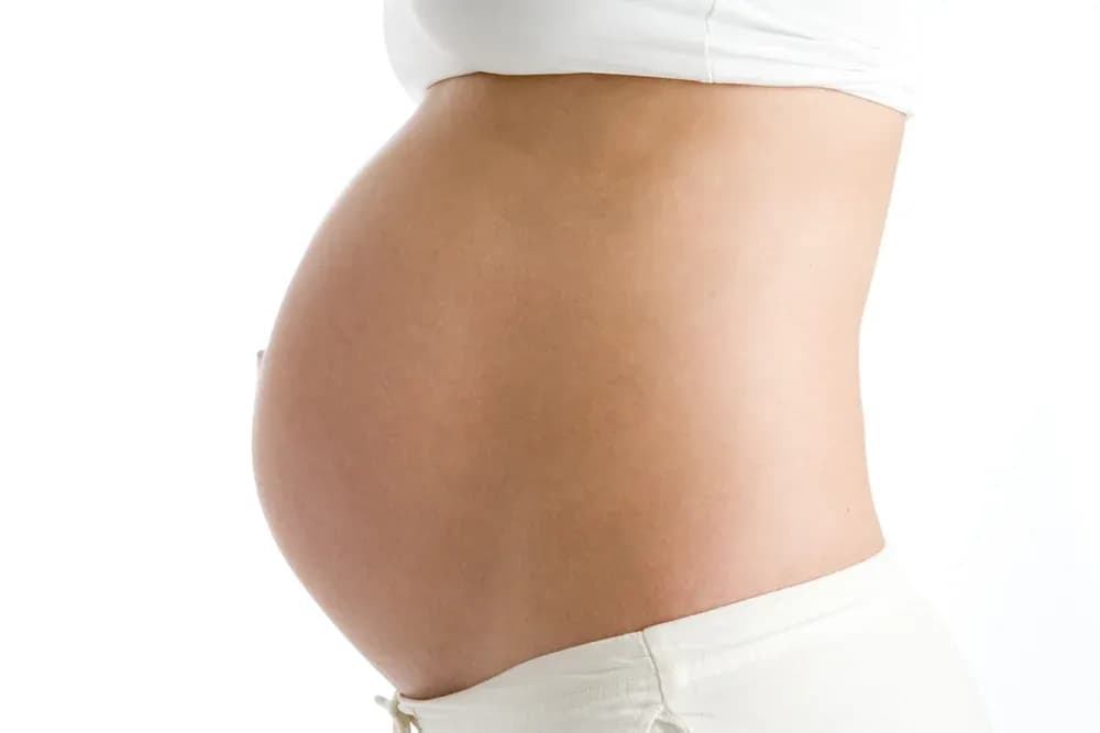 ventre de femme enceinte vu de profil vêtue de blanc