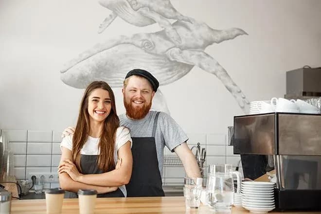 couple souriant derrière un comptoir de café avec des tasses et un décor mural artistique