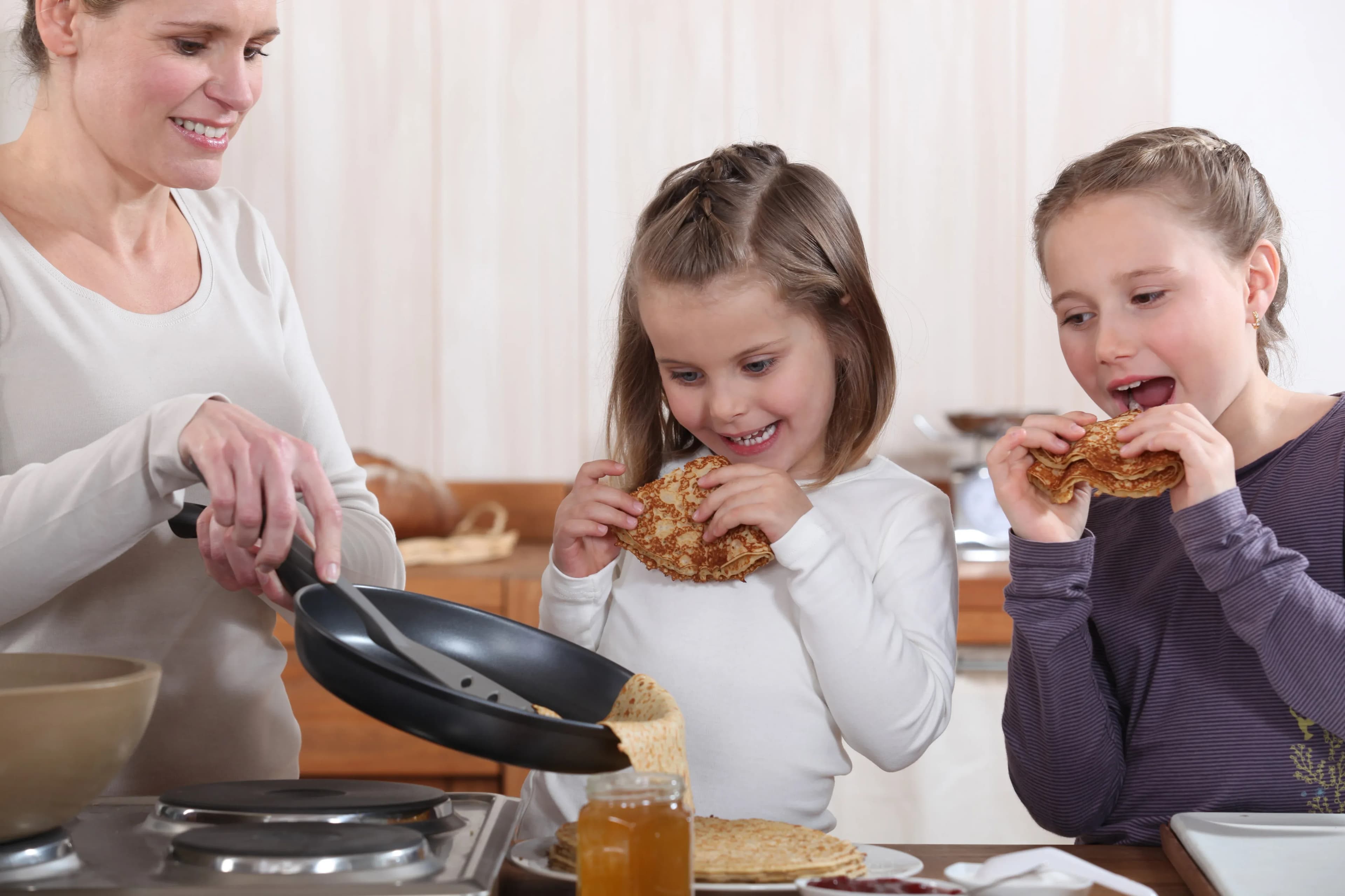 Préparation de crêpes en famille avec deux enfants souriants et une mère à la cuisine