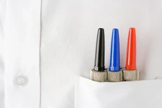trois marqueurs de couleurs noire bleue et rouge dans une poche de chemise blanche