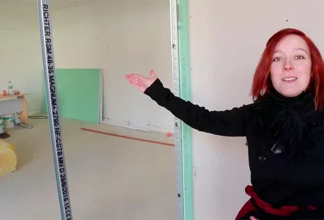 femme montrant un espace vide avec des murs en construction et des matériaux de rénovation