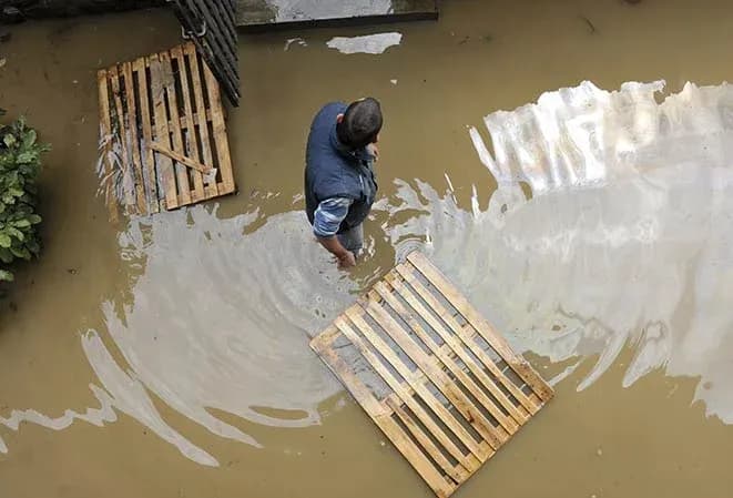 homme dans une zone inondée avec des palettes en bois flottant sur l'eau stagnante