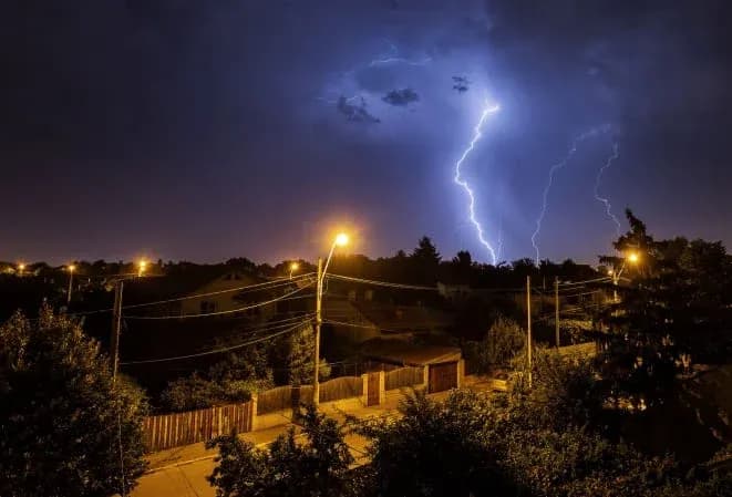 orage avec éclairs illuminant le ciel au-dessus d'un quartier résidentiel la nuit