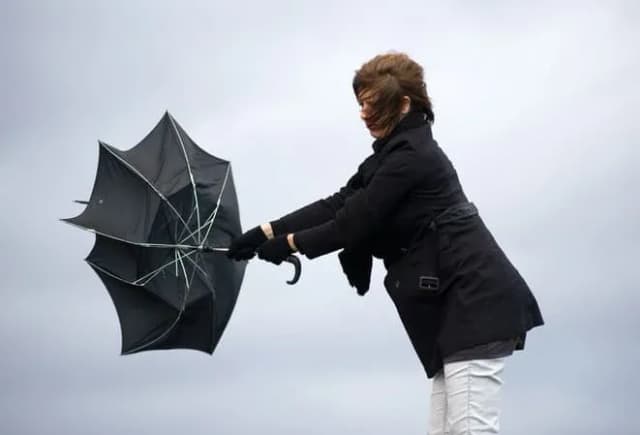 femme tenant un parapluie retourné par le vent sous un ciel nuageux