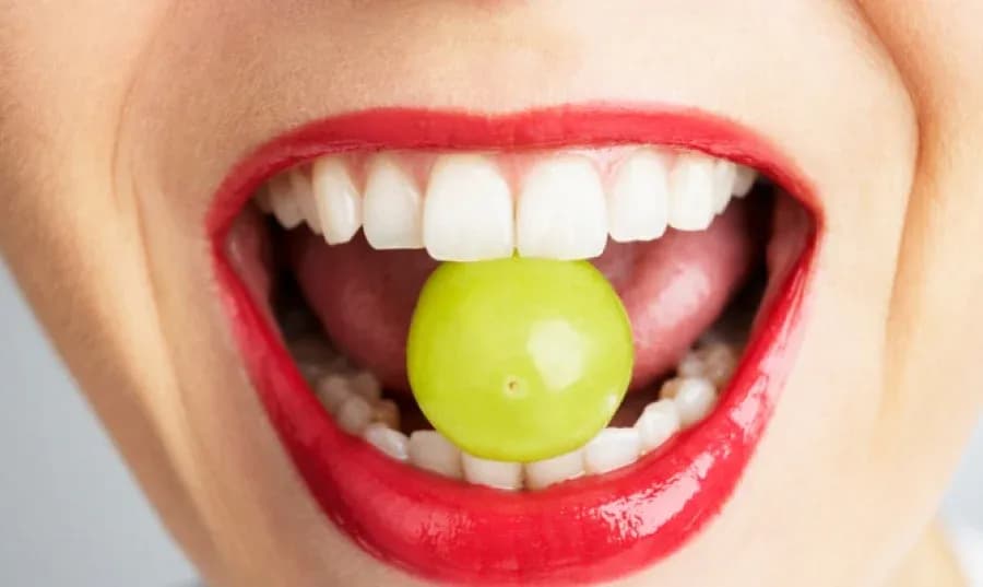 sourire avec des dents blanches et une grappe de raisin vert dans la bouche