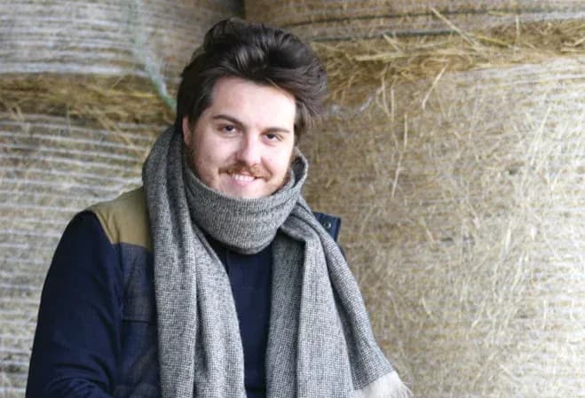 jeune homme souriant avec une écharpe dans un environnement rural avec des ballots de foin en arrière-plan