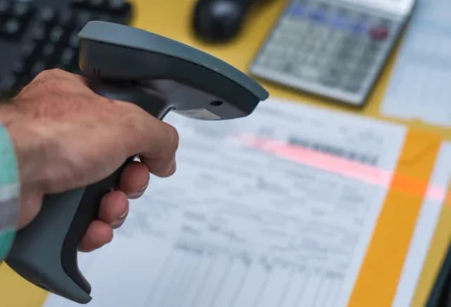 scanner en main sur un bureau avec des documents et une calculatrice en arrière-plan