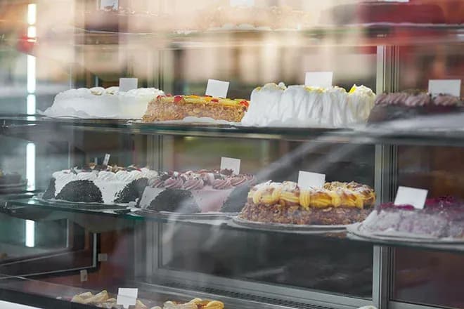 vitrine de pâtisserie avec plusieurs gâteaux décorés et étiquettes blanches