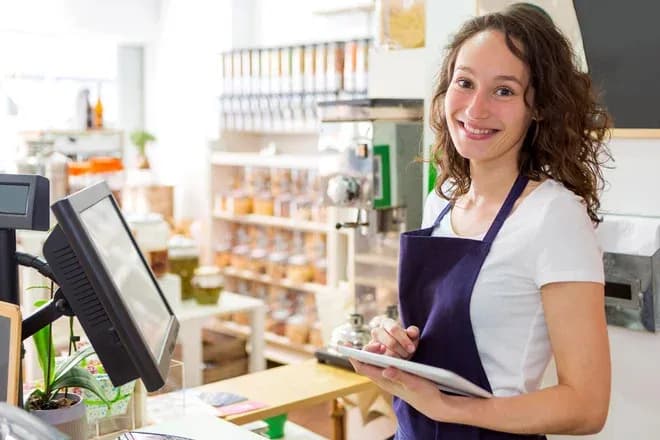 vendeuse souriante en tablier tenant une tablette devant le comptoir d'une épicerie