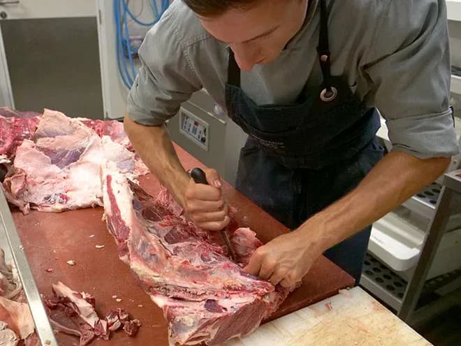 apprenti boucher désossant une pièce de viande sur plan de travail