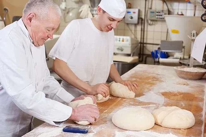 apprentis boulangers pétrissant de la pâte sur un plan de travail en cuisine professionnelle