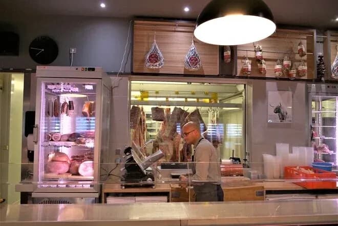 boucherie avec un employé utilisant une trancheuse devant des viandes exposées en vitrine