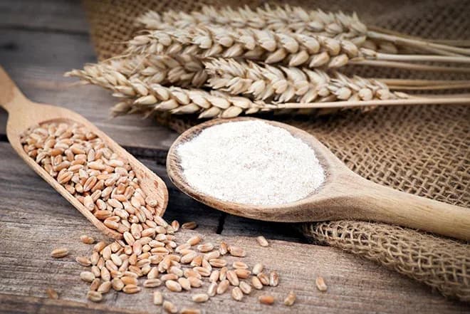 grains de blé et farine dans des cuillères en bois sur une toile de jute