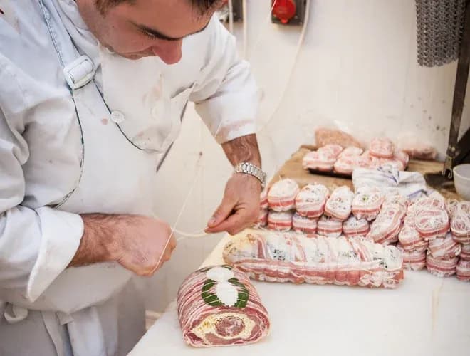 charcutier nouant des rôtis et pièces préparées sur un plan de travail