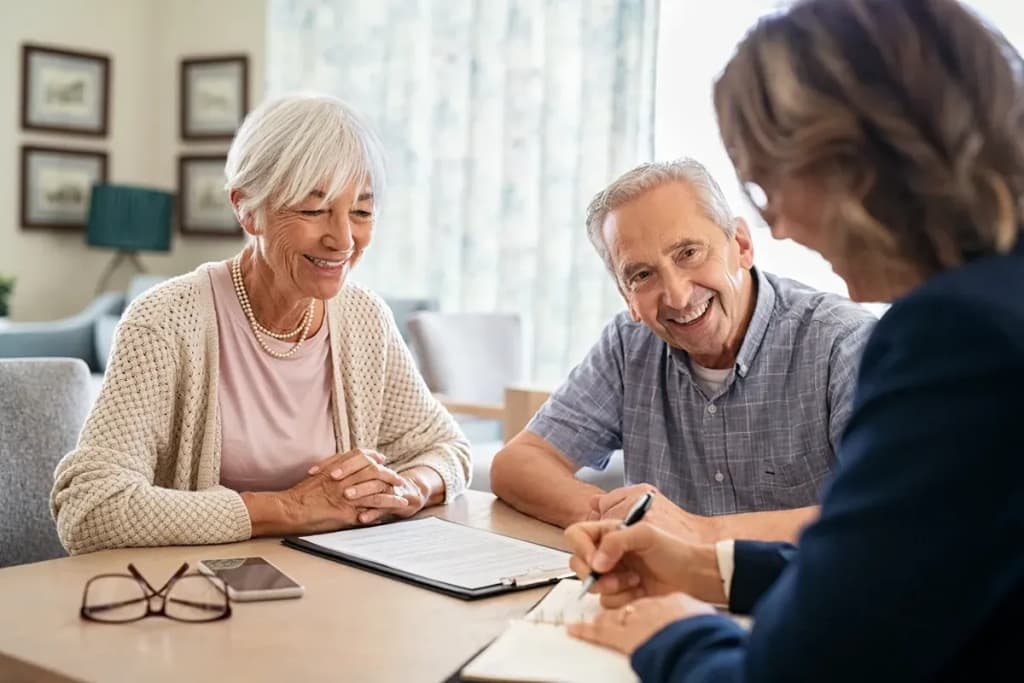 Couple de seniors souriants assis face à un conseiller qui remplit un document sur une table