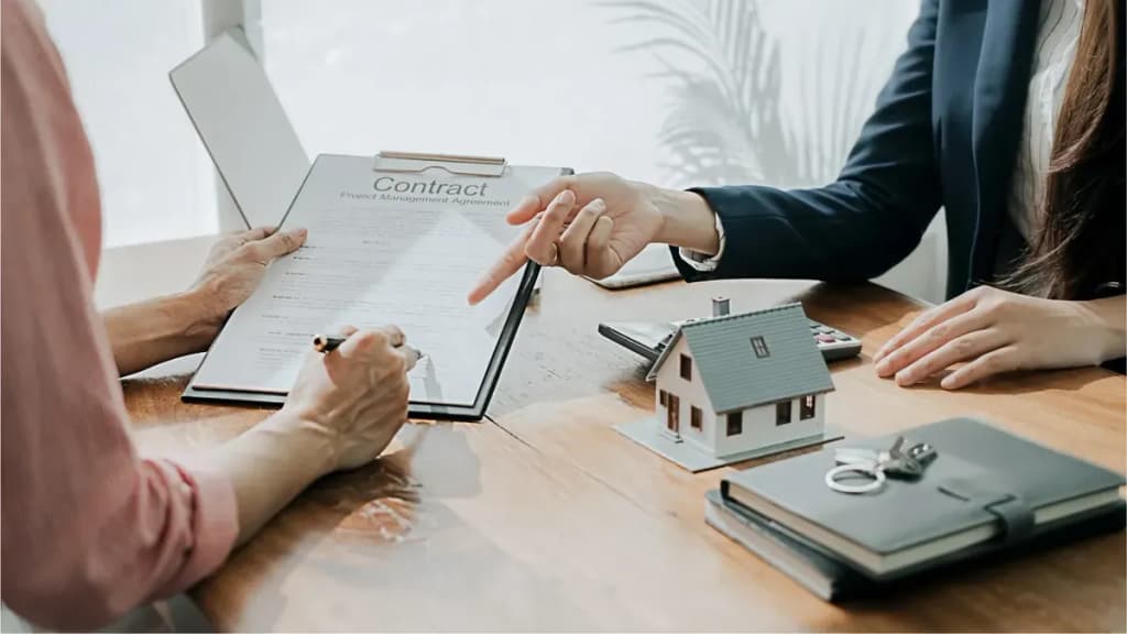 Deux personnes signent un contrat immobilier autour d'une table avec une maquette de maison et des clés
