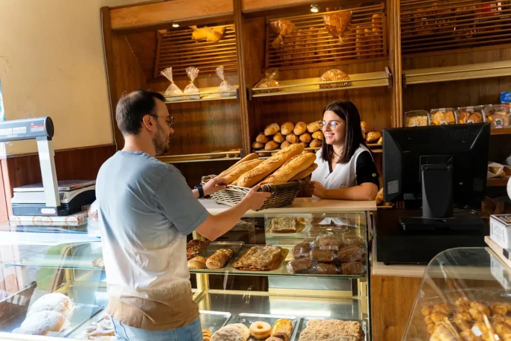 Boulangère souriante tendant un panier de baguettes à un client au comptoir d'une boulangerie