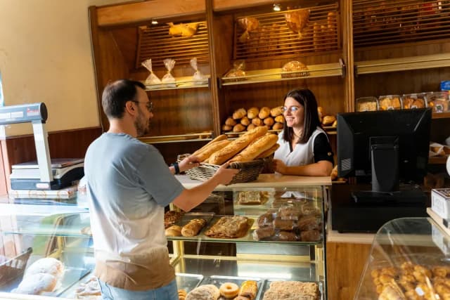 Boulangère souriante tendant un panier de baguettes à un client au comptoir d'une boulangerie