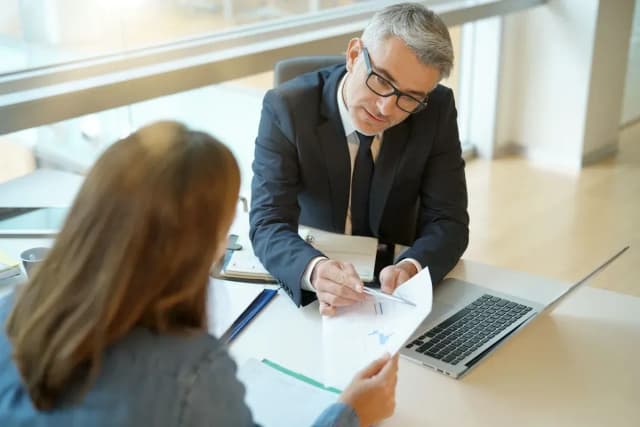 Un conseiller en costume montre un document avec des graphiques à une cliente lors d'un rendez-vous professionnel
