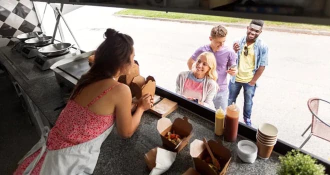vendeuse d'un food truck remettant des plats à trois clients souriants