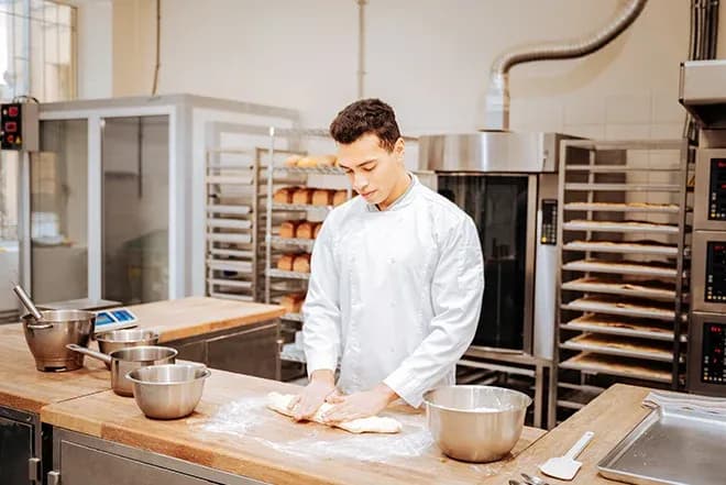 apprenti boulanger pétrissant une pâte dans une cuisine professionnelle équipée