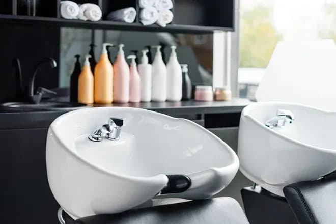 bac à shampoing blanc avec des bouteilles de produits capillaires en arrière-plan