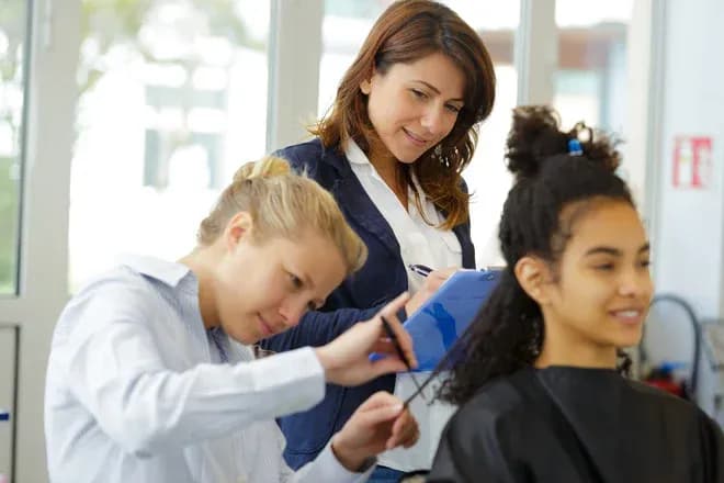 apprentie coupe les cheveux d'une cliente sous la supervision d'une formatrice