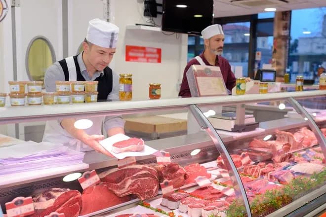 Deux bouchers au comptoir vitré présentant différents morceaux de viande