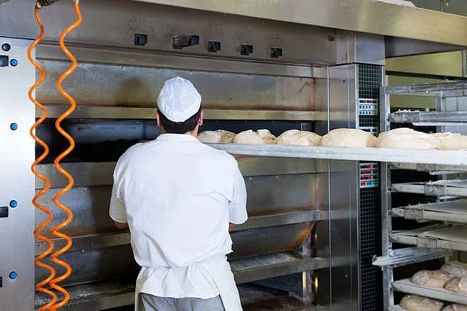 boulanger en blouse blanche place des pâtons dans un four professionnel