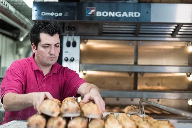 boulanger range des pains chauds sur un comptoir devant un four industriel