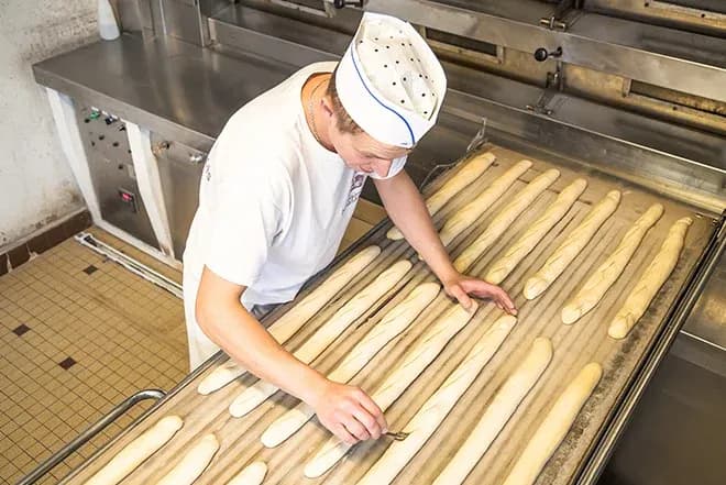 boulanger en toque incisant des baguettes avant cuisson