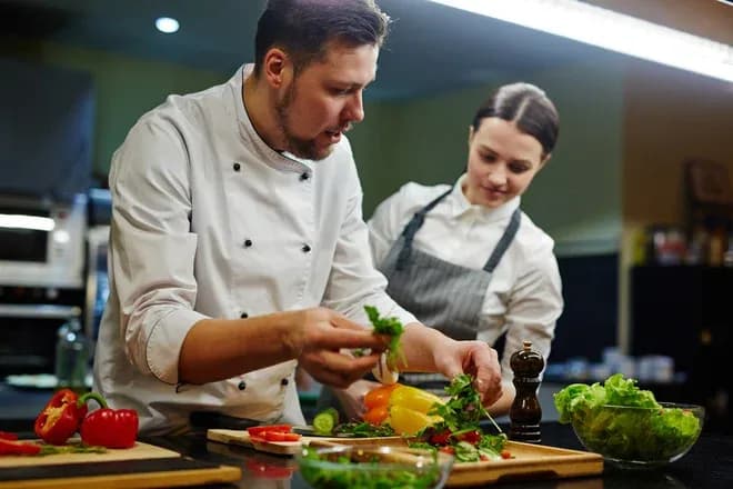 chef formateur montrant la préparation d'une salade à une apprentie en cuisine