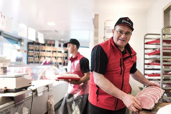 deux bouchers en gilet rouge préparant des tranches de viande au comptoir