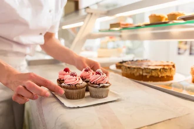 pâtissier posant des cupcakes sur un plateau dans une vitrine de pâtisserie