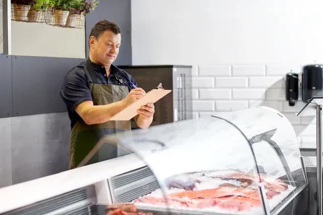 Homme souriant prenant des notes devant un comptoir de poissonnerie avec des produits frais