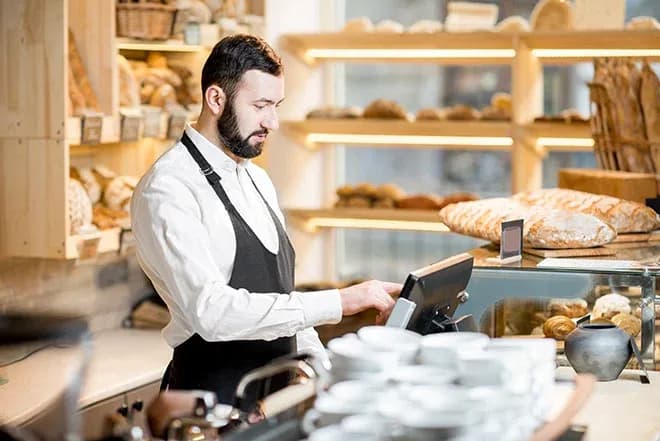 Employé de boulangerie utilisant une caisse enregistreuse avec des pains en arrière-plan