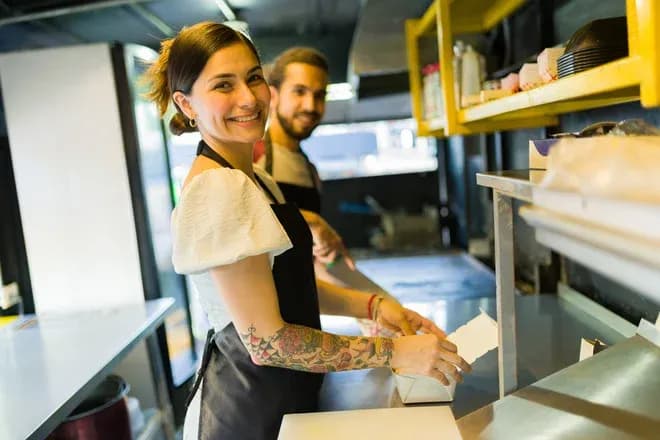 employée souriante bras tatoué préparant un repas à emporter dans un camion-restaurant