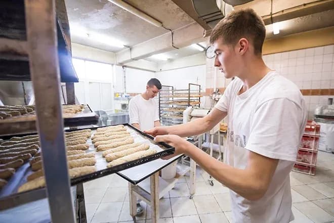 apprenti boulanger prépare des pâtons sur une plaque dans le fournil