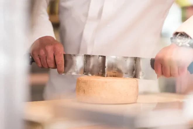 fromager en blouse blanche coupant une meule de fromage avec un fil