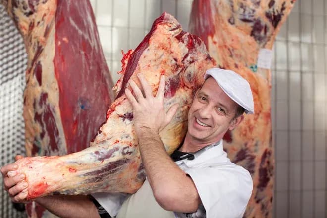 boucher souriant portant une grosse pièce de viande dans une chambre froide carrelée