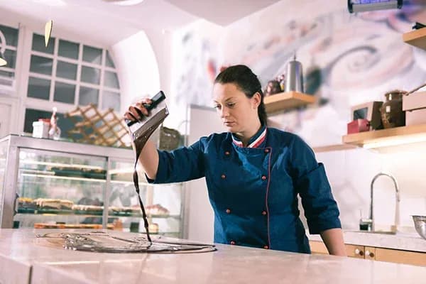 femme en tenue de pâtissière verse du chocolat sur un plan de travail dans une chocolaterie