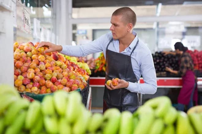 Homme choisissant des fruits dans un marché avec des étals colorés en arrière-plan