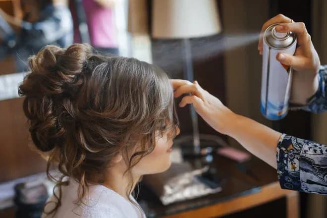 Coiffeur appliquant un spray sur les cheveux d'une cliente en coiffure élégante
