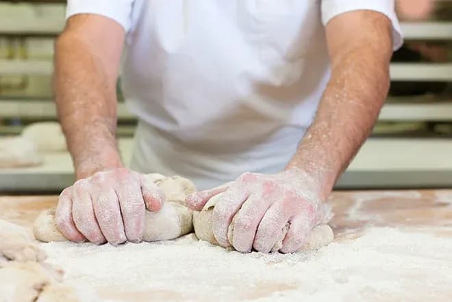 Mains pétrissant de la pâte sur un plan de travail fariné dans une boulangerie