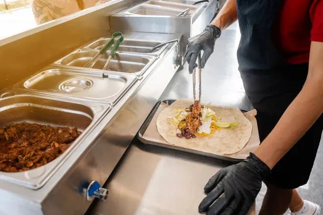 personnel ganté préparant un wrap avec viande et garnitures dans un food truck