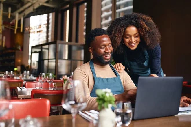 personnes souriantes travaillant sur un ordinateur portable dans un restaurant moderne