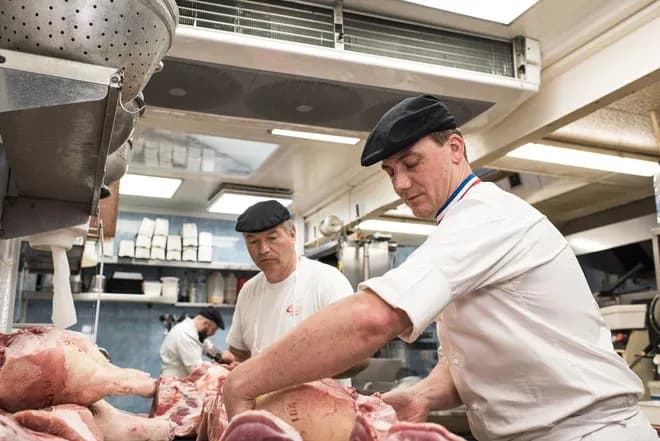Deux bouchers en train de préparer de la viande dans un atelier de charcuterie